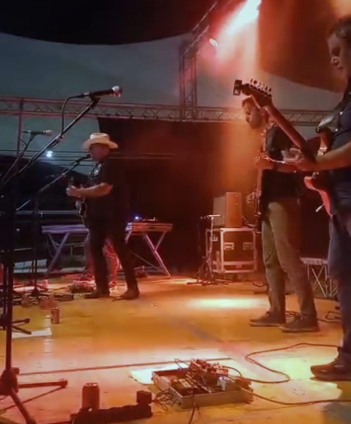 Tullo e i Rebel Hot su un palco all’aperto, di sera, sotto le luci arancioni