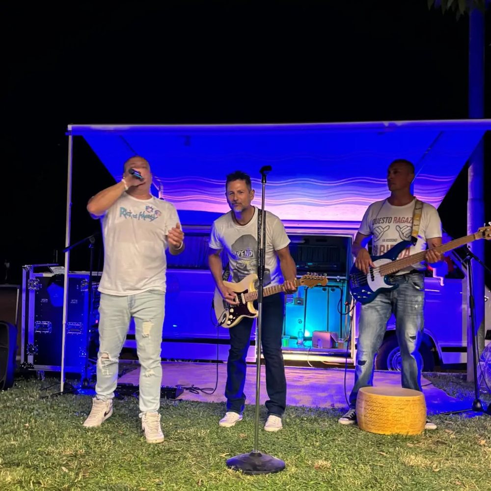 Il gruppo sul palco di sera, luci blu, il cantante con il microfono in mano e gli altri due alle chitarre