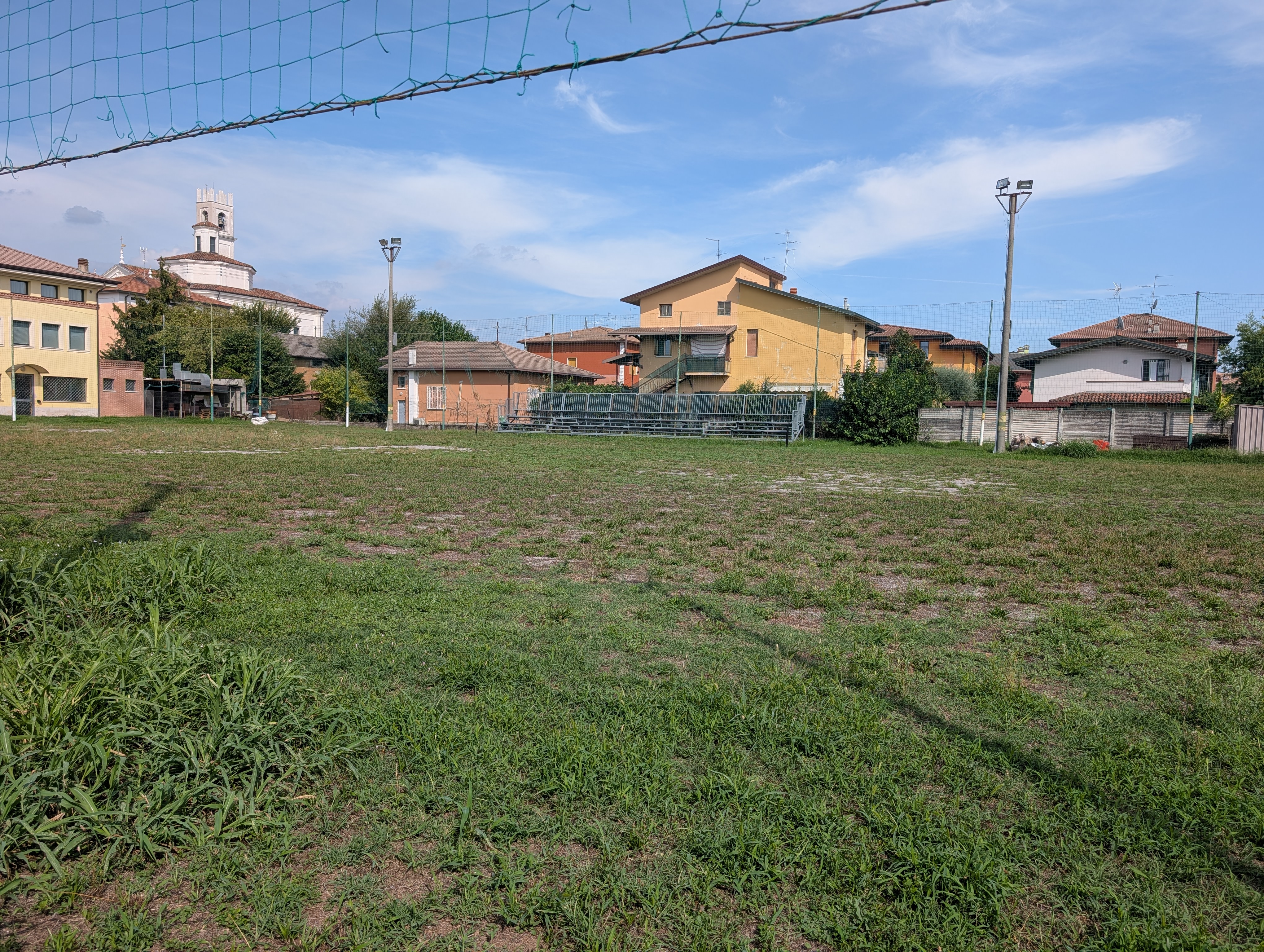 Il campo sportivo dietro l’oratorio, con la rete, la tribuna e il campanile di Folzano sullo sfondo