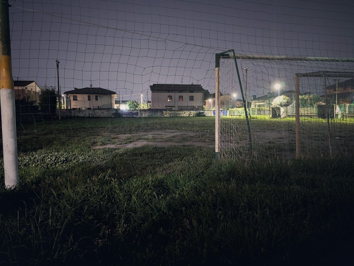 Il campo sportivo dietro l’oratorio di sera, con la porta e l’erba alta sotto i lampioni del quartiere