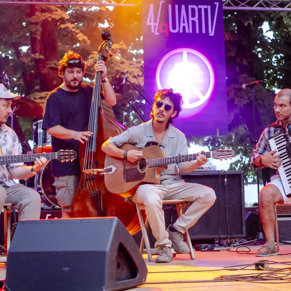 Il gruppo che suona su un palco all'aperto, di sera, con le luci colorate