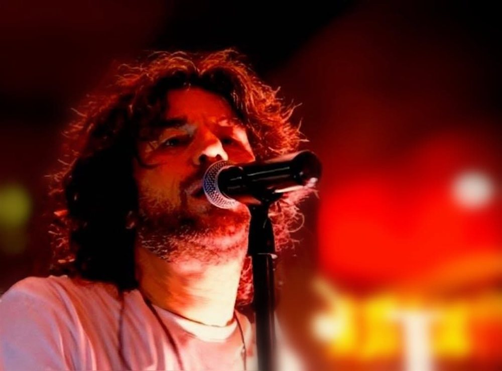 Roberto Guolo con il microfono in mano, illuminato da luci rosse di scena