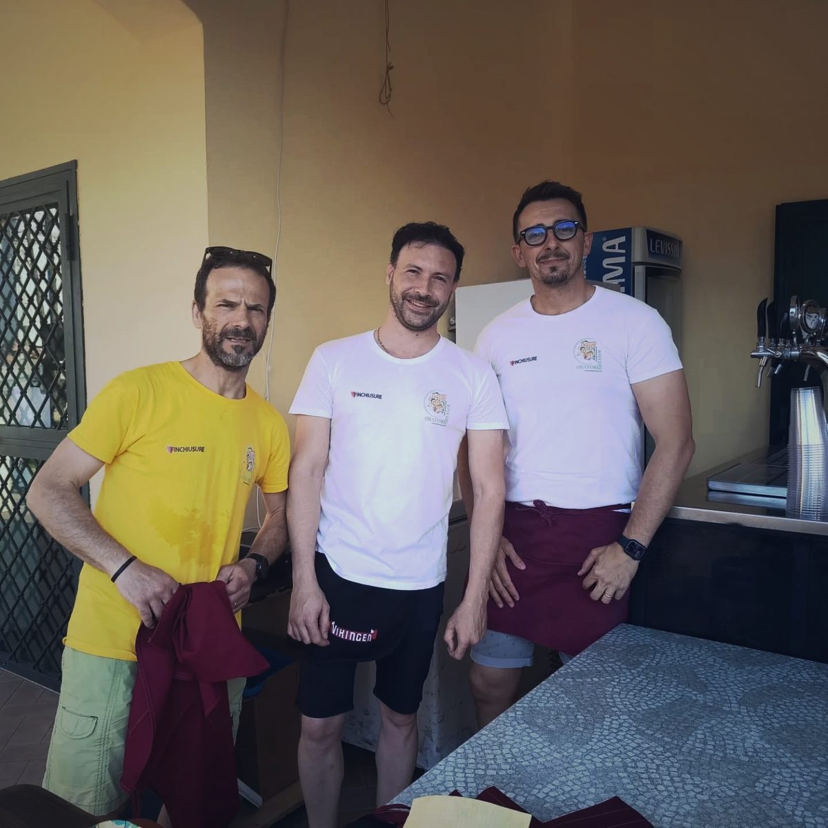 Tre volontari dietro al bancone del bar dell’oratorio, con le spine della birra