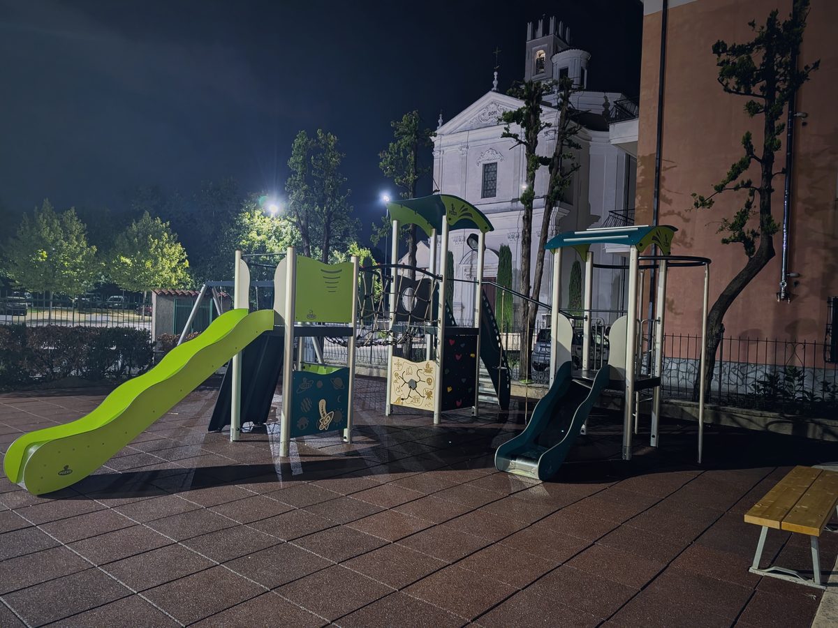 Lo spazio giochi dell’oratorio di sera, con lo scivolo verde e la facciata della chiesa sullo sfondo