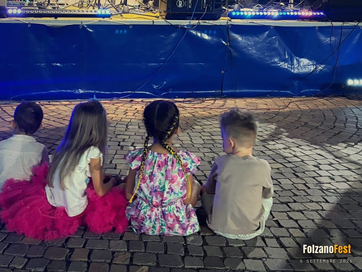 Quattro bambini seduti in terra davanti al palco, prima che cominciasse